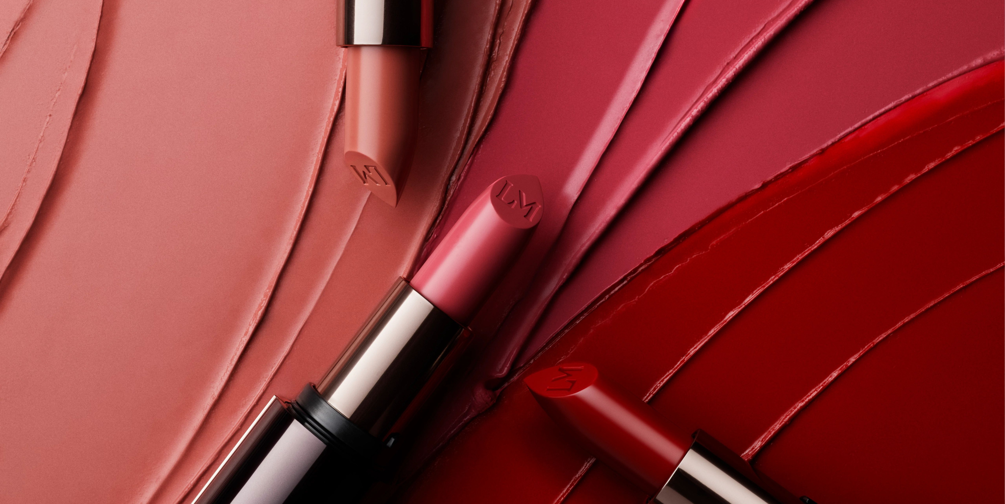 Laura Mercier's Caviar Hydra-Creme lipsticks on top of a gradient swatch of beige, pink, and red