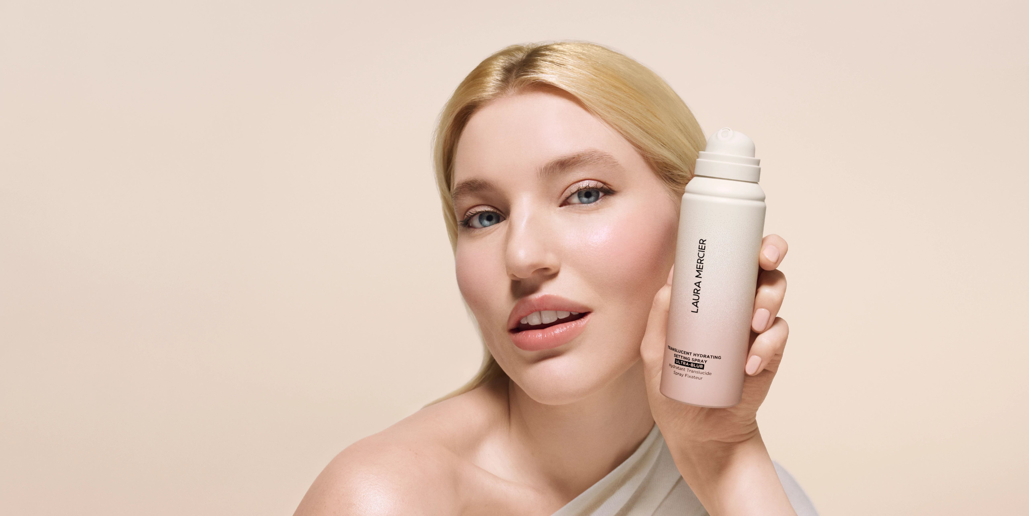 Blonde pale model holding up Laura Mercier's Translucent Hydrating Setting Spray Ultra-Blur