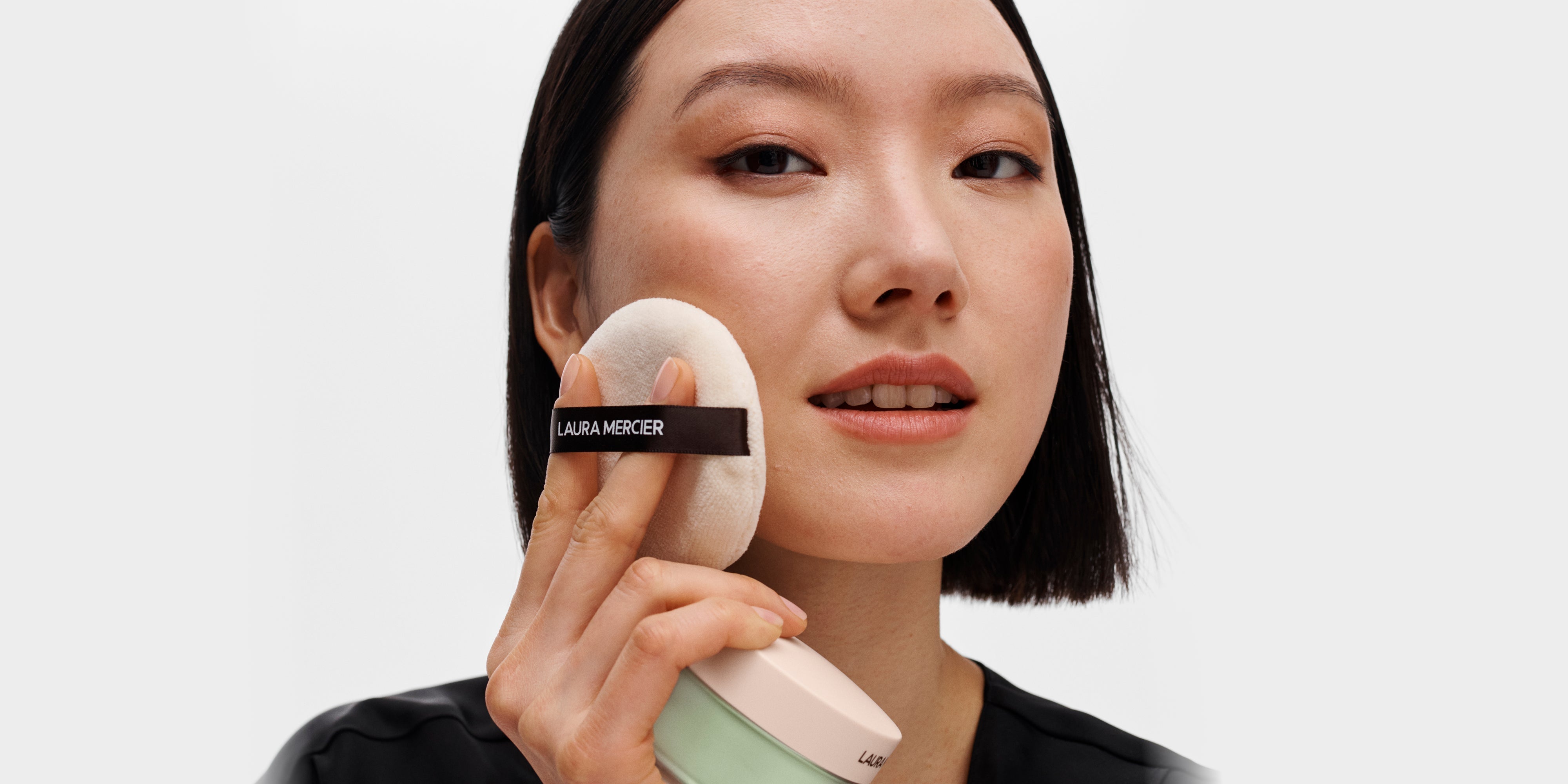 Model applying Ultra Blur Translucent Loose Setting Powder in Mint Shade with Laura Mercier Velour Puff